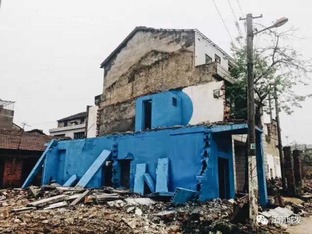 △ 這棟建筑是臨江最近的半拆遷建筑物的遺留，沅江和堤壩成為了展覽的天然背景。創(chuàng)作團(tuán)隊(duì)對這棟建筑進(jìn)行了半涂裝，將符號性的沅水曲線與拆遷進(jìn)行中的建筑立面進(jìn)行意義的疊造，它們共同觸發(fā)了場所空間多元語境的生成，把拆遷這種暫時破壞性、干擾性的介入行動與沅水右岸發(fā)展的未來性、美好性緊密融合。